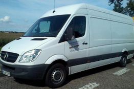 Weißer Lieferwagen der Marke Mercedes parkt auf einer Straße bei klarem Himmel.