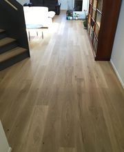 Helles Wohnzimmer mit Holzboden, Treppe links, Bücherregal rechts und Sofa im Hintergrund.