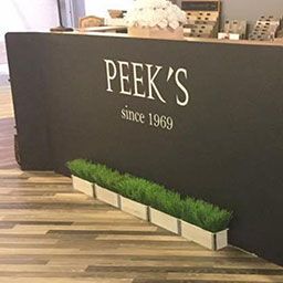 Sign reading "Peek's since 1969" with planters in front on a wooden floor.