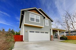 Two-story gray house with a garage, large driveway, and clear blue sky background.