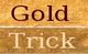 Text-Grafik mit den Wörtern "Gold" in braun und "Trick" in beige auf Holzstruktur.