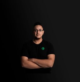 Eine Person mit Brille in schwarzem T-Shirt vor einem dunklen Hintergrund, die Arme verschränkt.