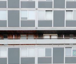 Wohnblock mit grauen Fassaden. Balkon mit Holzverkleidung und brasilianischer Flagge im Fenster.