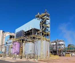 Usina industrial com tanques e estrutura metálica sob céu azul claro.