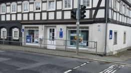 Fachwerkhaus mit Versicherungsbüro, Bürgersteig und Ampel bei bedecktem Himmel.