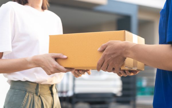 Ein Paketbote überreicht einer Frau ein Paket, das als Expresslieferung versandt wurde.