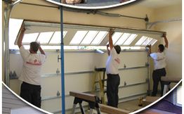 Three workers installing a garage door panel in a garage.