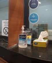 Recepção vazia com balcão, telefone, cartazes, álcool gel e caixa de máscaras sobre a mesa.