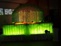 Grüne Hochzeitstafel mit Lichterketten und Luftballons dekoriert.