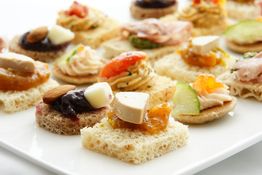 Assortiment de canapés variés sur un plateau blanc, garnis de fromage, fruits secs et légumes.