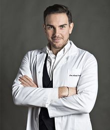 Uomo in camice bianco, con le braccia incrociate, sfondo grigio.