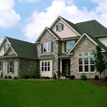 A large stone and brick house with a green lawn and partly cloudy sky in the background.