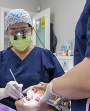 Dentista atiende a un paciente en el consultorio, asistida por otro profesional de salud.