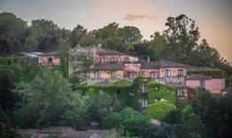 Complesso di edifici rosa antico tra colline verdi al tramonto.