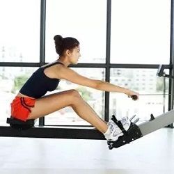 Frau trainiert auf einem Rudergerät in einem Fitnessstudio mit großen Fenstern.