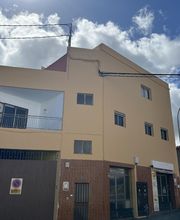 Edificio amarillo en esquina con cielo nublado y cables eléctricos visibles.