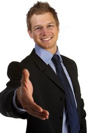 Geschäftsmann im Anzug lächelt und streckt die Hand aus, als wollte er jemanden begrüßen.