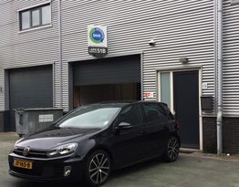 Zwarte auto geparkeerd voor een bedrijfsgebouw met een bord dat "DHZ" aangeeft.