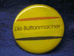 Gelber Button mit der Aufschrift "Die Buttonmacher", zwei diagonale Linien.