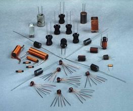 Verschiedene elektronische Bauteile, darunter Spulen und Kondensatoren, auf grauem Untergrund.