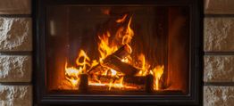 Open haard met brandend hout en vlammen, geplaatst in een stenen muur.