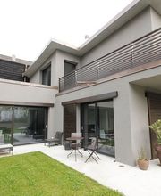 Modernes Haus mit Terrasse, Balkon, Rasen und Pflanzen, graue Fassade und Holzverkleidung.