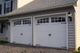 White double garage doors with decorative windows on a white house, exterior light fixtures mounted.