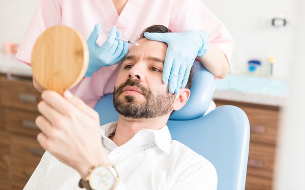 Ein Patient, der sich während der Botulinumtoxin-Therapie im Spiegel betrachtet.