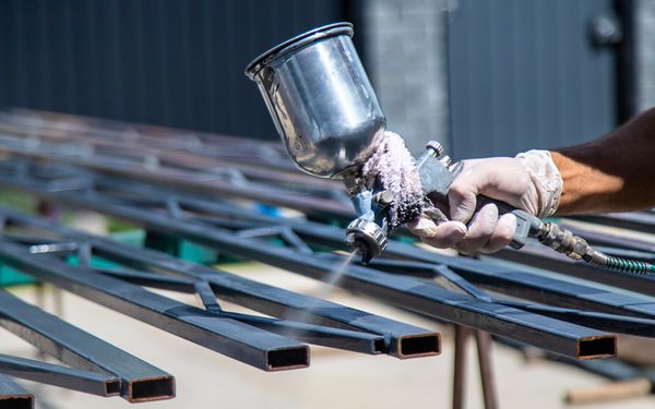 Ein Mann besprüht ein Metallteil mit einer speziellen schwarzen Pulverbeschichtung.