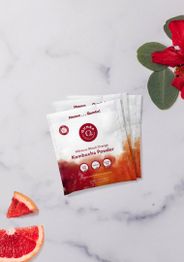 Kombucha powder packets with hibiscus, orange slices, and a flower on a marble surface.