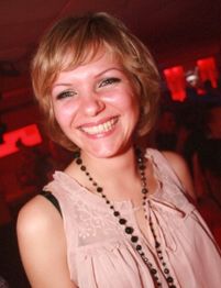 Eine lächelnde Frau in einem rosa Oberteil in einem rot beleuchteten Raum.