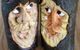 Zwei geschnitzte Gesichter in Holzscheiten, nebeneinander mit weißen und orangefarbenen Details.
