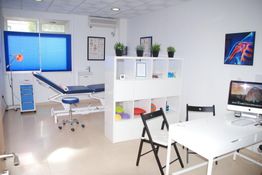 Consultorio médico moderno con camilla, escritorio y decoración sencilla.