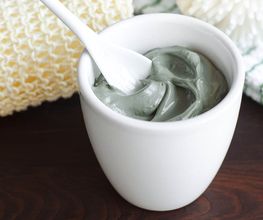 Crema grigia in un vasetto bianco con cucchiaino, accanto a una spugna gialla.