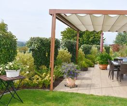 Überdachte Terrasse mit Esstisch, umgeben von grünen Pflanzen und gepflegtem Garten.