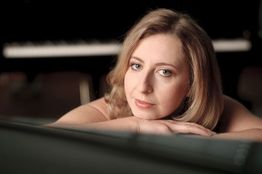 Frau mit blondem Haar liegt nachdenklich auf einem Klavier, unscharfes Klavier im Hintergrund.