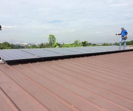Personas instalando paneles solares en un techo bajo un cielo nublado.
