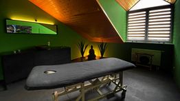 Massageraum mit schwarzer Liege, grünen Wänden, Buddha-Statue und stimmungsvollem Licht.