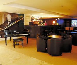 Sala de estar elegante com piano preto, cadeiras de couro, bar e imagem de homem na parede.