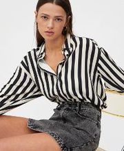 Mujer sentada con camisa de rayas blancas y negras, y falda gris. Fondo blanco.