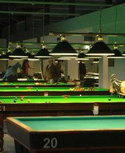 Mehrere Snooker-Tische mit Spielern in einem beleuchteten Raum.
