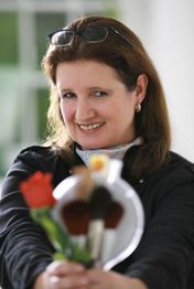 Eine lächelnde Frau hält Pinsel und eine rote Rose in der Hand.