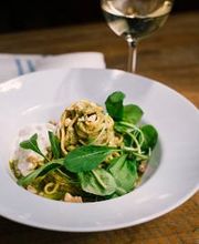 Prato de massa com vegetais e queijo, acompanhado de uma taça de vinho branco sobre a mesa.