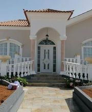 Fachada de una casa con techo rojo, puerta blanca y jardín al frente.