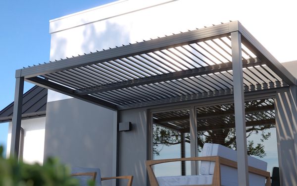 Eine anthrazit farbene Pergola mit Lamellendach, über einer Terrasse, montiert an einer Hauswand.