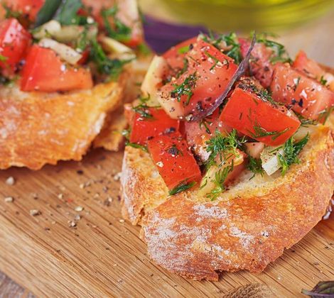Bruschetta con pomodori freschi, cipolla e erbe su tagliere di legno.