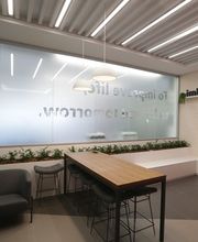 Sala moderna com mesa alta, bancos e sofá. Placas de vidro com letreiro e plantas decorativas.