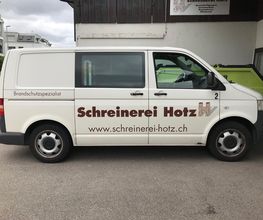 Weißer Lieferwagen mit der Aufschrift "Schreinerei Hotz" und "Brandschutzspezialist" an der Seite.