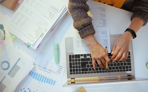 Steuerberaterin am Laptop von oben. Steuerunterlagen liegen auf dem Schreibtisch.