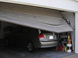 Car stuck under a partially closed garage door in a cluttered garage.